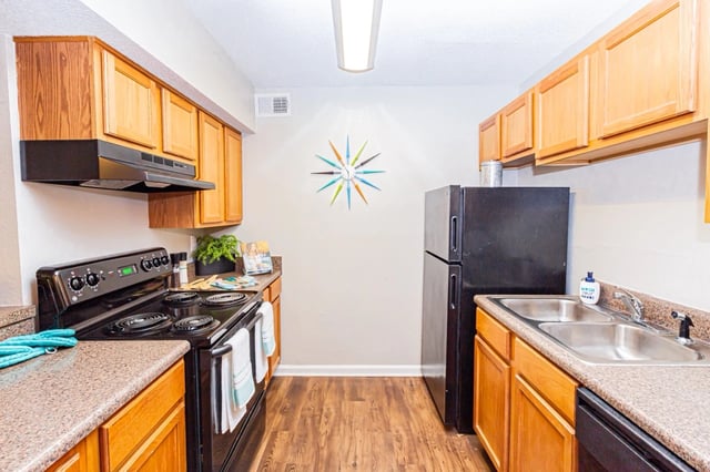 Kitchen with black appliances, wooden cabinets, and speckled countertops.