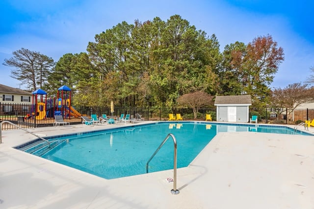 Outdoor swimming pool with lounge chairs and a playground in the background.