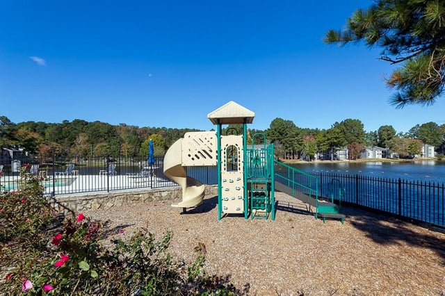 Playground with slides and climbing wall next to a lake and swimming pool.