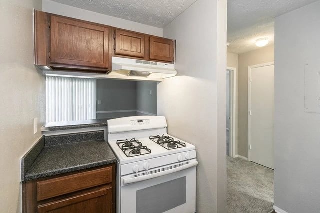 White gas range with a dark countertop and wooden cabinets in a kitchen.