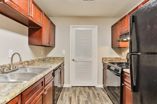Kitchen with cherry cabinets, granite countertops, stainless steel sink, and black appliances.