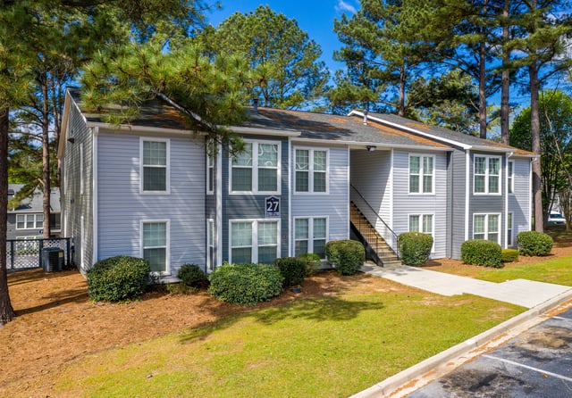 Exterior view of apartment building with blue and grey siding, stairs, and surrounding greenery.