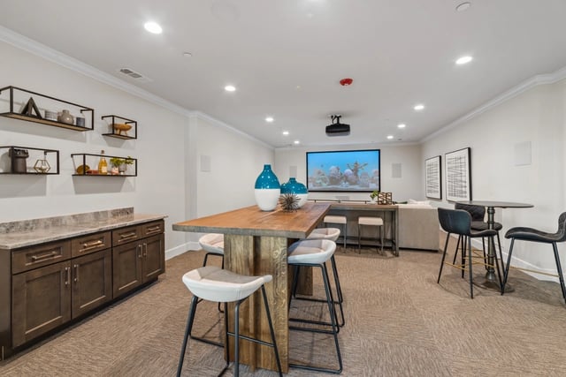 Community lounge area with a large screen for movie viewing, a bar with stools, and high-top tables.