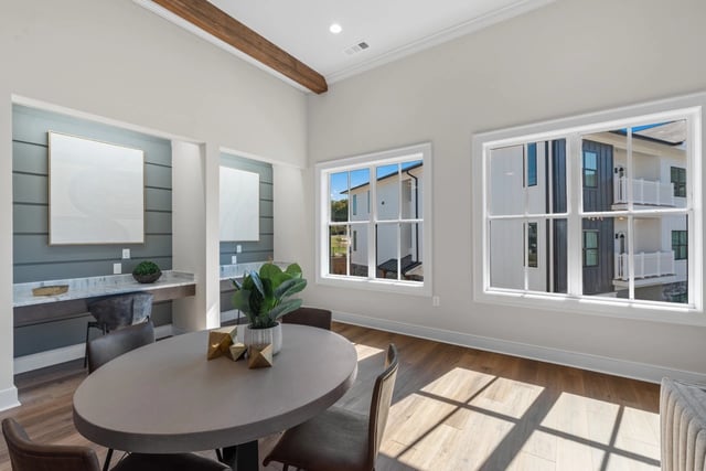 Interior of a community lounge area with a table and chairs, looking out windows to apartment buildings.