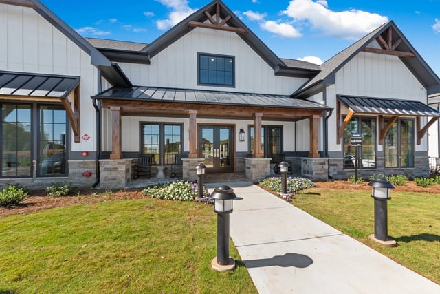 Exterior of a modern farmhouse style apartment building with a welcoming porch and landscaping at The Blakely in Pendergrass, GA.