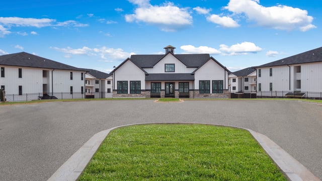 Modern apartment buildings with a central clubhouse under a blue sky with clouds at The Blakely in Pendergrass, GA.
