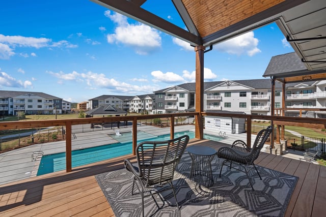 View of a swimming pool and apartment buildings from a balcony with chairs at The Blakely, offering apartments in Pendergrass, GA.
