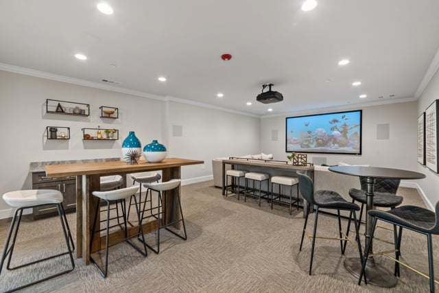 Community lounge area with a bar, high-top tables, and a large projector screen showing an aquarium at The Blakely, offering apartments in Pendergrass, GA.