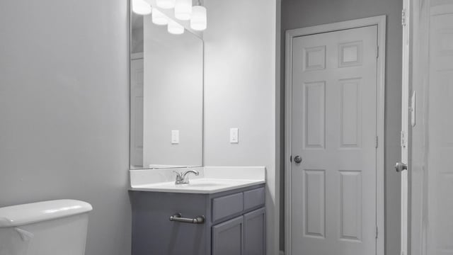Bathroom vanity with sink, mirror, and toilet in apartment.