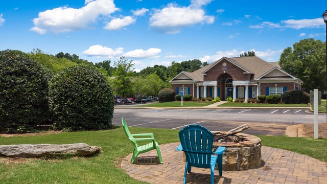 Outdoor seating area with chairs around a fire pit, next to a brick building with blue shutters.