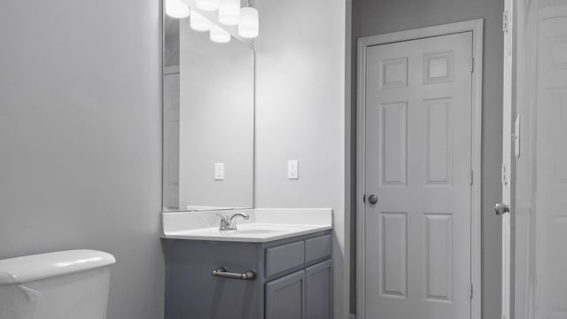 Bathroom vanity with sink and mirror, next to a closed door and a toilet.