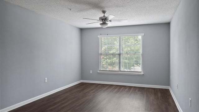 Empty apartment bedroom with gray walls, ceiling fan, and wood-look flooring.