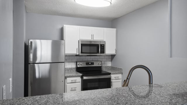 Kitchen with stainless steel appliances including a refrigerator, microwave, and oven, as well as white cabinets and granite countertops.