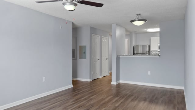 Living area with wood floors, ceiling fan, and view into kitchen.