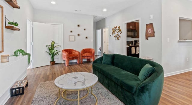 A modern living room with a deep green sofa and two orange accent chairs.