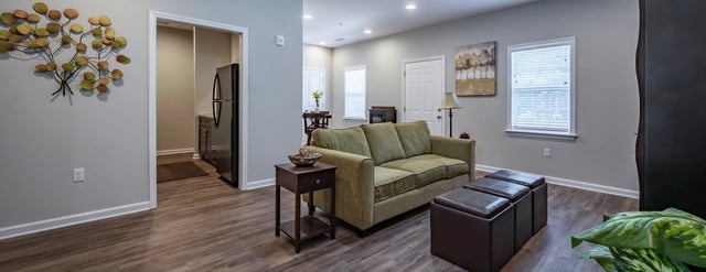 Living room with a green sofa, ottoman, side table, and kitchen view.