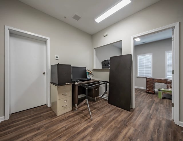 Office space with a desk, computer, filing cabinet, and printer. Adjacent room visible.