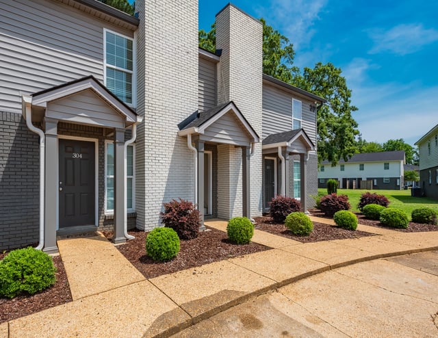 Exterior of apartment buildings with manicured bushes and trees.