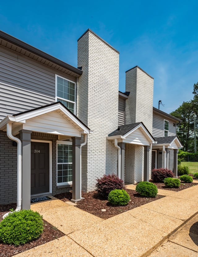 Exterior view of apartment buildings with gray siding and white brick accents, featuring dark doors and manicured landscaping.