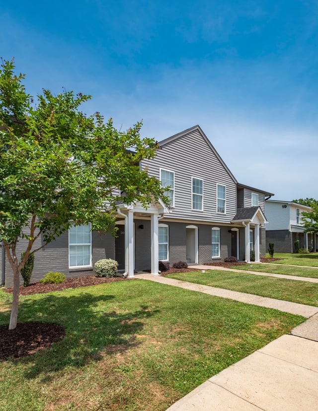 Exterior view of townhome apartments with grey siding and dark grey brick on a sunny day.