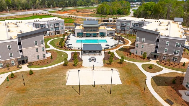 Aerial view of apartment buildings with a pool, volleyball court, and outdoor seating areas.