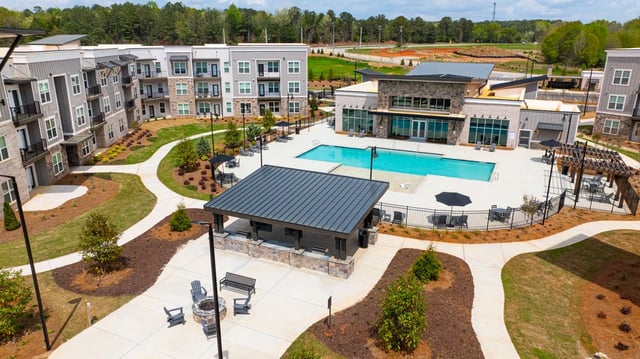 Aerial view of a modern apartment complex with a large swimming pool, outdoor lounge area, and building exteriors.