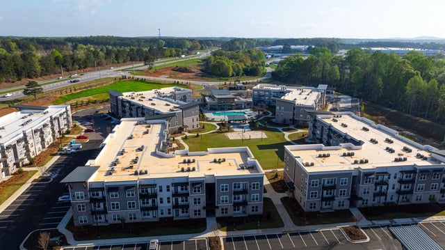 Aerial view of modern apartment buildings with a swimming pool and green spaces in the center.
