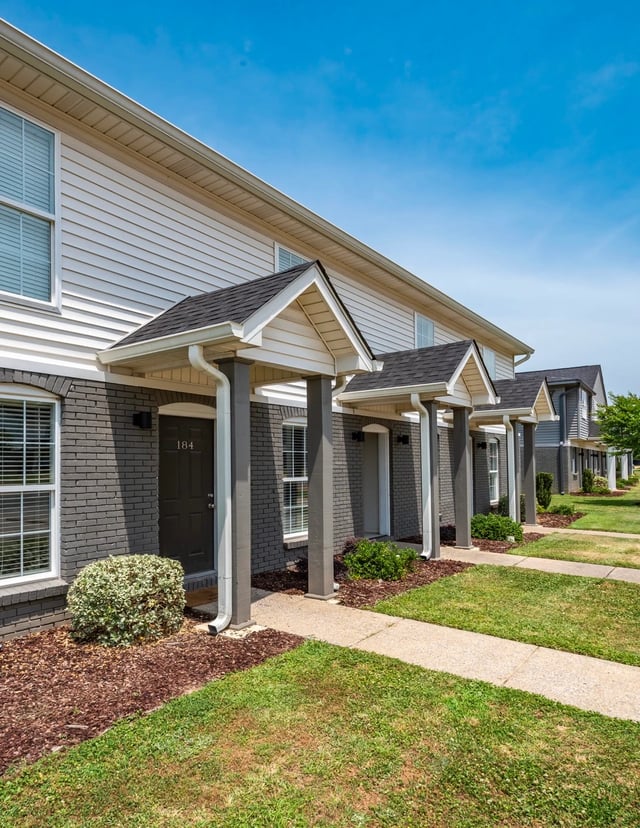 Exterior view of apartment buildings with covered entryways and sidewalks.