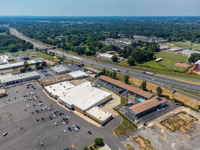 Aerial view of apartment buildings, a swimming pool, and surrounding commercial properties near a highway.