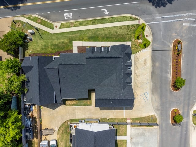 Aerial view of a multifamily property with dark shingles, showing surrounding roads and landscaping.