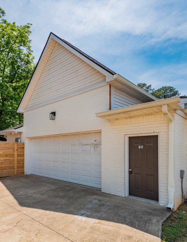 Exterior of a white brick building with a large garage door and a brown side door, under a bright blue sky.