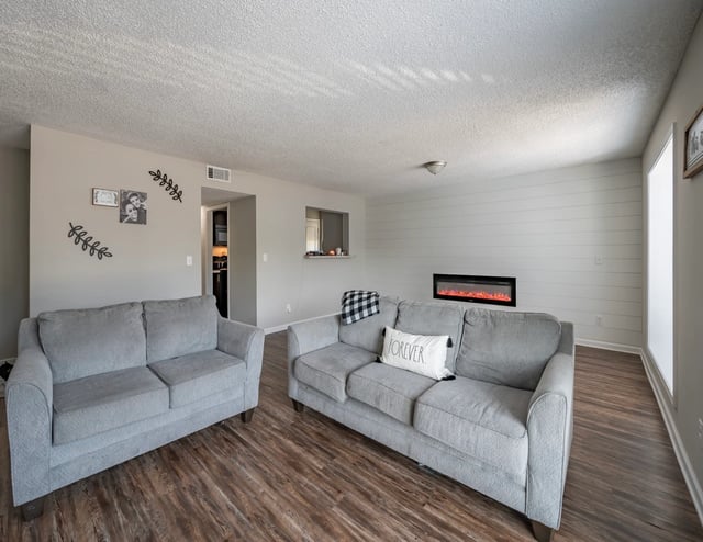 Cozy living room with two gray sofas, a modern electric fireplace, and wood-look flooring.