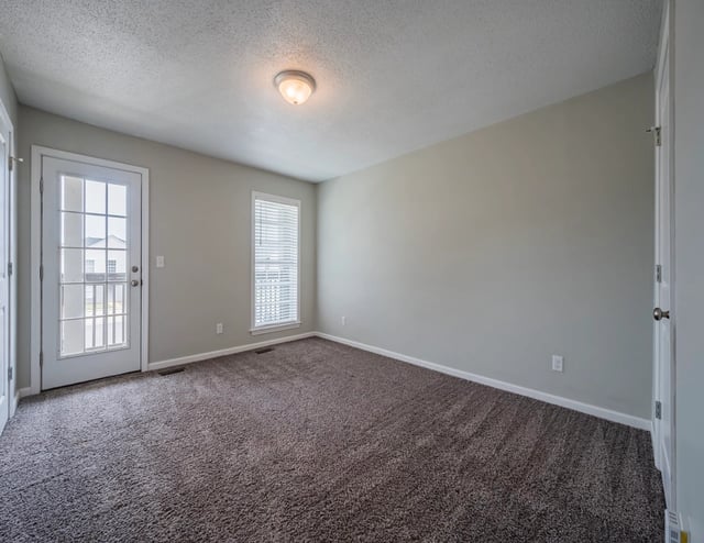 Empty living room with carpet, blinds, and a glass door leading to a porch.