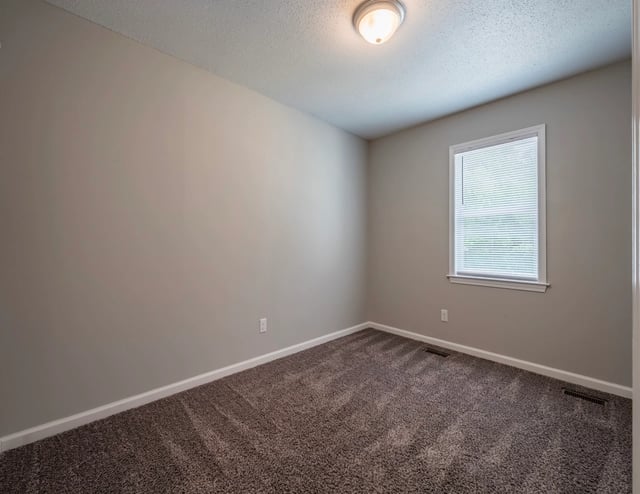 Empty bedroom with neutral walls, carpet, and a single window with blinds.