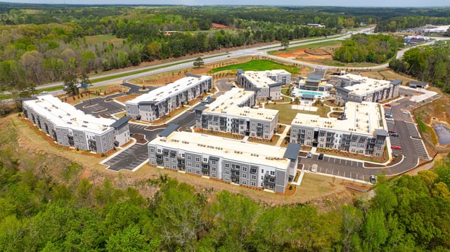 Aerial view of an apartment complex with multiple buildings, parking lots, and a swimming pool.