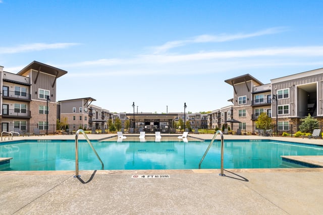Outdoor swimming pool with lounge chairs and a covered cabana area, surrounded by apartment buildings.