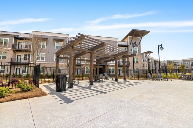 Outdoor seating area with pergola and lounge chairs in front of apartment buildings.