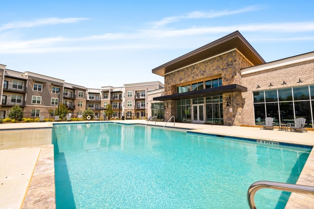 Luxury apartment complex with a large, sparkling blue swimming pool in the foreground and modern buildings in the background.