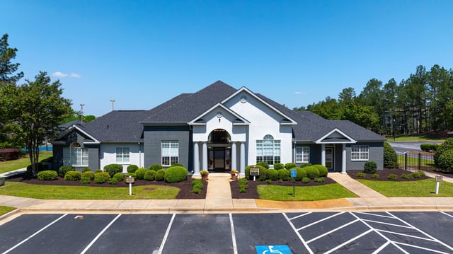 Exterior view of the leasing office building with manicured bushes and parking lot.