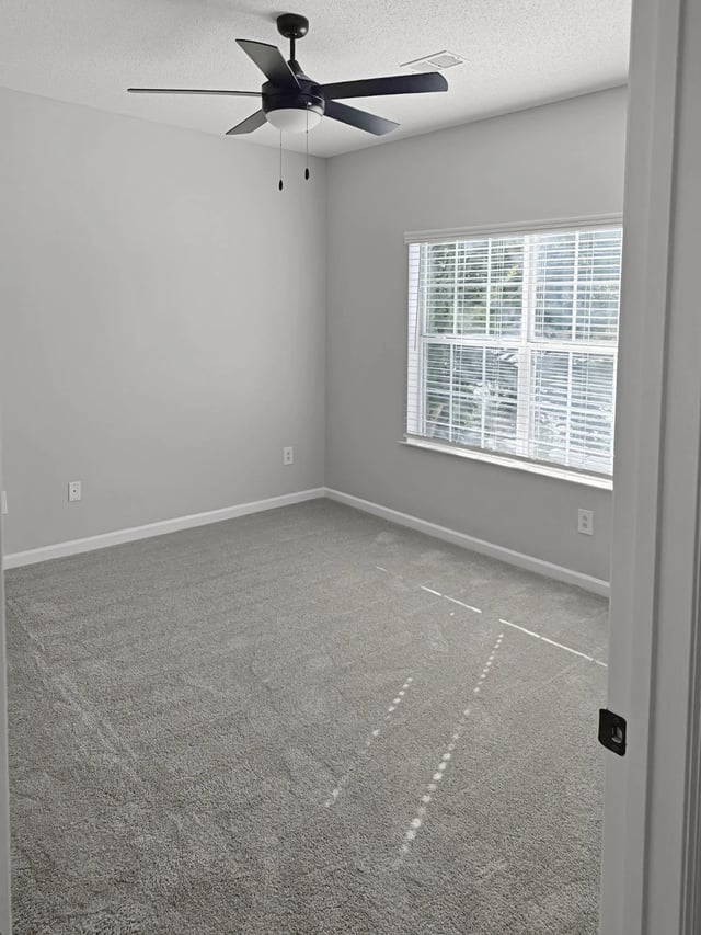 Bedroom with carpet, ceiling fan, and window with blinds.