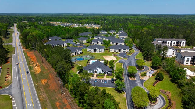 Aerial view of a multifamily property with multiple buildings, a pool, tennis court, and volleyball court.