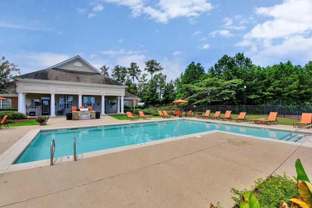 Resort-style swimming pool with lounge chairs and umbrellas outside a clubhouse.