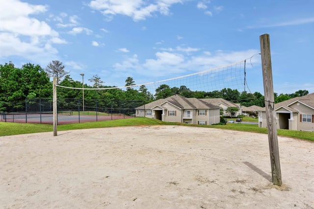 Sand volleyball court with a net, tennis court and apartment buildings in the background.