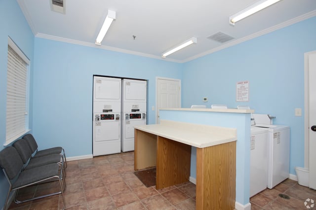 Laundry room with stacked washers and dryers, seating area, and folding counter.