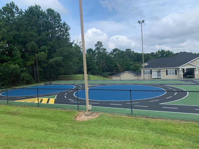Outdoor play area with a track for toy cars, surrounded by fencing and trees.