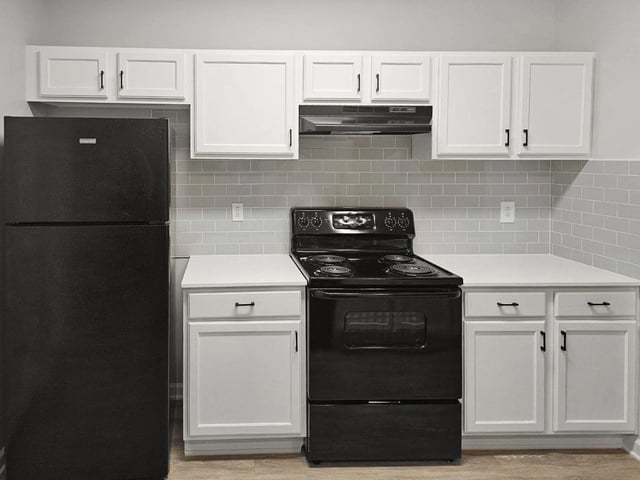 Modern kitchen with white cabinets, white countertops, black refrigerator, and black oven.