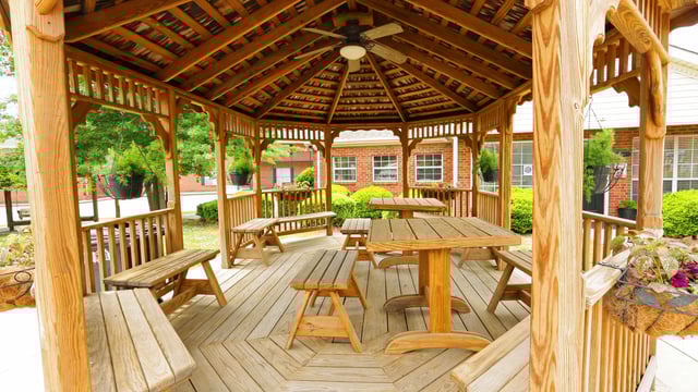 Wooden gazebo with picnic tables and benches in a courtyard setting.