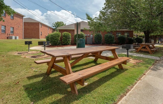 Picnic tables and grills in a grassy courtyard area with brick buildings in the background.