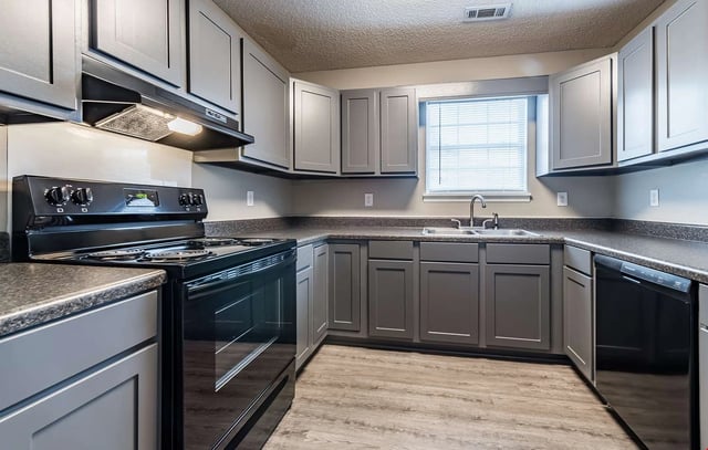 Modern kitchen with gray cabinets, black appliances, and granite countertops.
