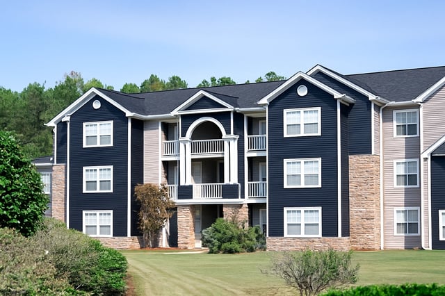 Exterior of a multi-story apartment building with dark blue siding and beige accents, featuring balconies and manicured lawn.